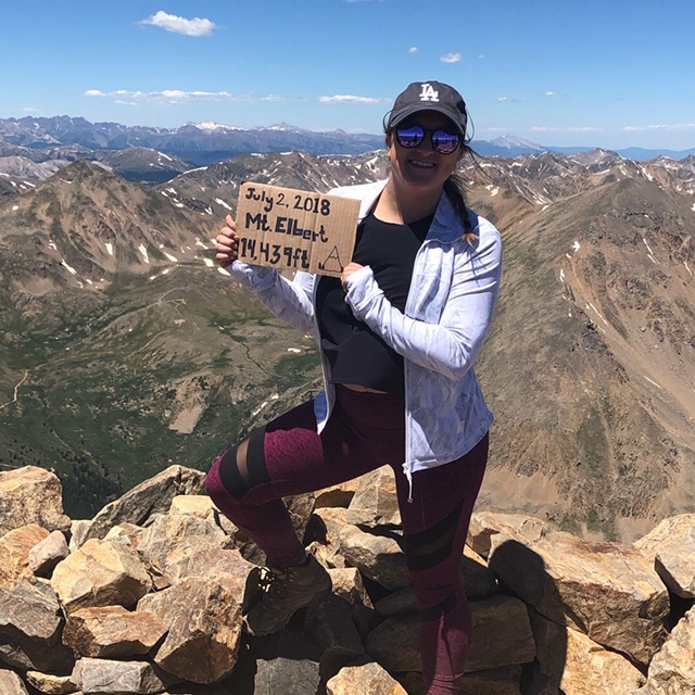 woman on top of mountain holding a sign