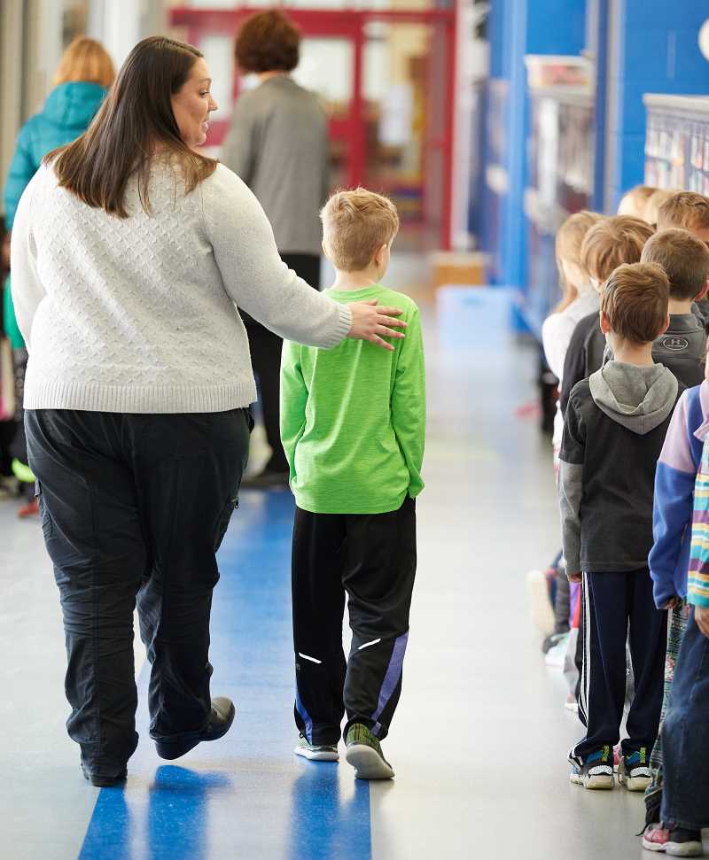 A school psychologist walks with a student in a school hallway.