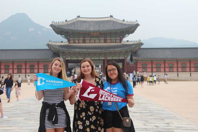 Three smiling students stand in front of a temple during their time at Hansung University in Seoul, South Korea