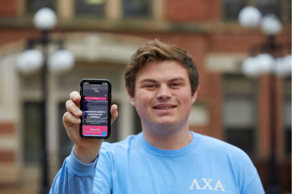 Chase Lehman of Lamda Chi poses with his cell phone, promoting the "Emma Loves Dogs" event and fundraiser. 