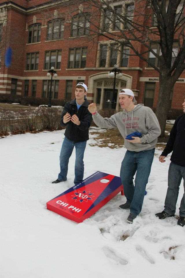 Two members of Chi Phi play bag toss outside in the snow. 