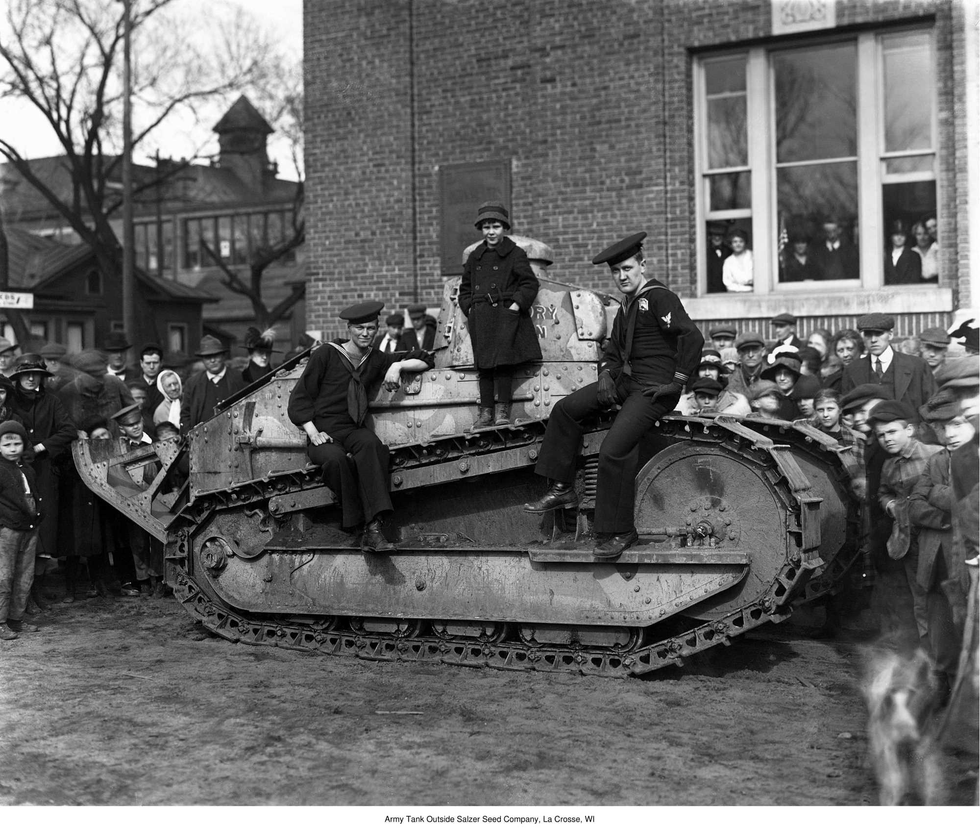 Black and white photograph featuring a view of US Navy sailors with an Army tank at the Salzer Seed Company on the corner of Seventh and Adams Streets in La Crosse, WI, April 12, 1919.