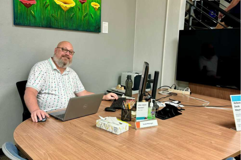 Scott Pfitzinger, Technology and Reference Services Librarian, sitting at the new Research and Reference Assistance Desk Location