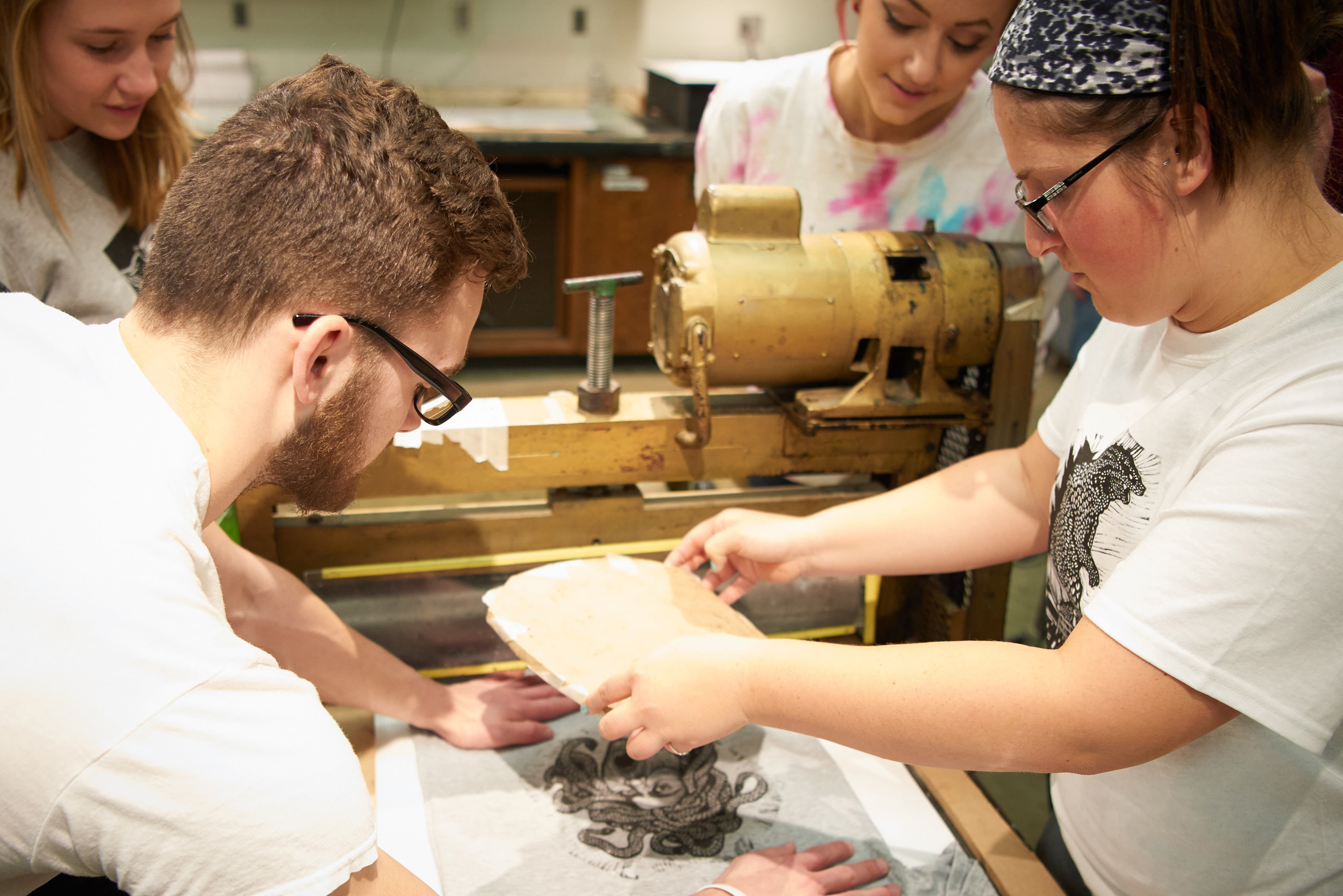 Printmaking students carefully remove the inked block off a t-shirt to reveal the printed artwork. 