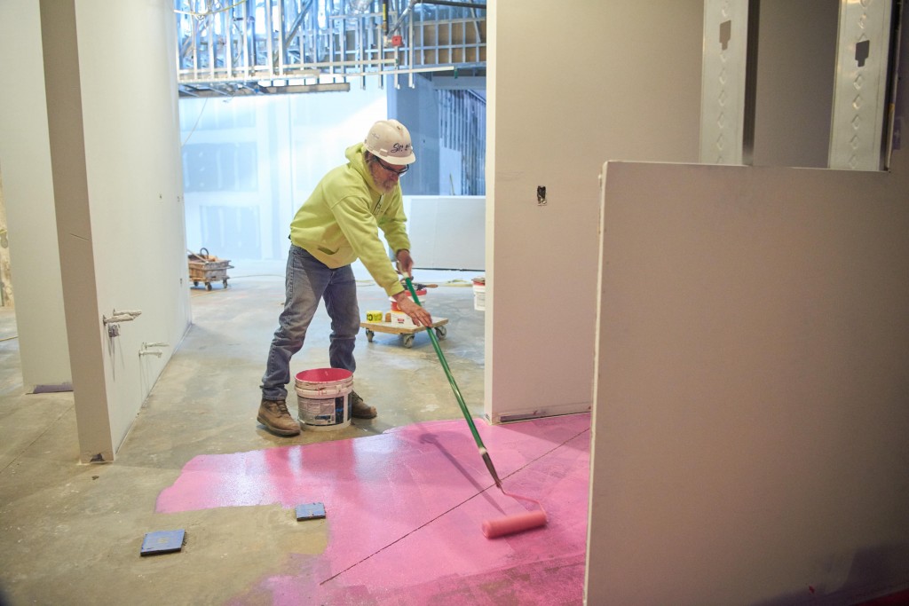 A worker prepares the floor with a waterproof coating before tile installation.