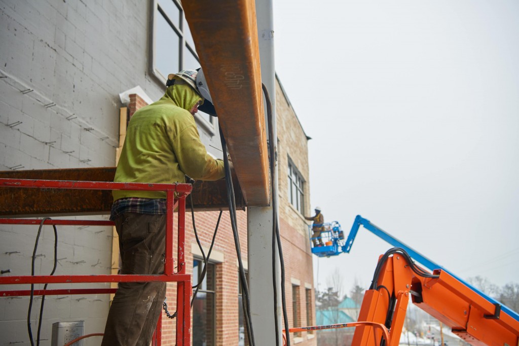 A contractor inspects a weld on a steel beam on the east side of the student center.