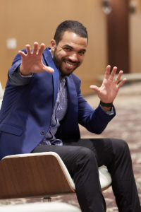 Jones sits and waves his hands in a mystical manner to the camera.