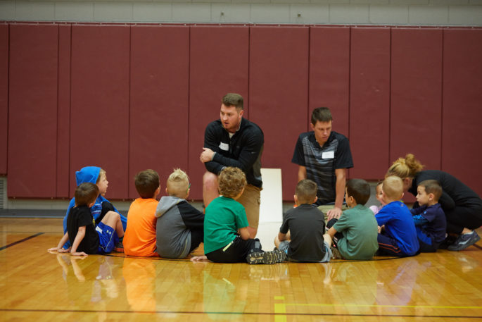 School-age children sit in a semi-circle around two UWL students.