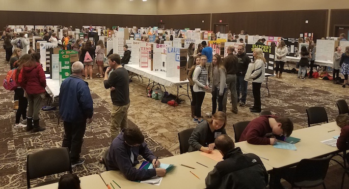 Image of The Bluffs overlooking a room filled with students giving poster presentations.