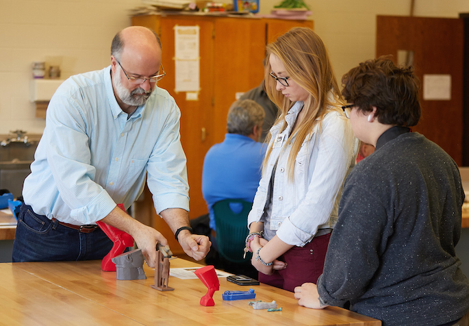 David Anderson showing 3D models to two students at a table.