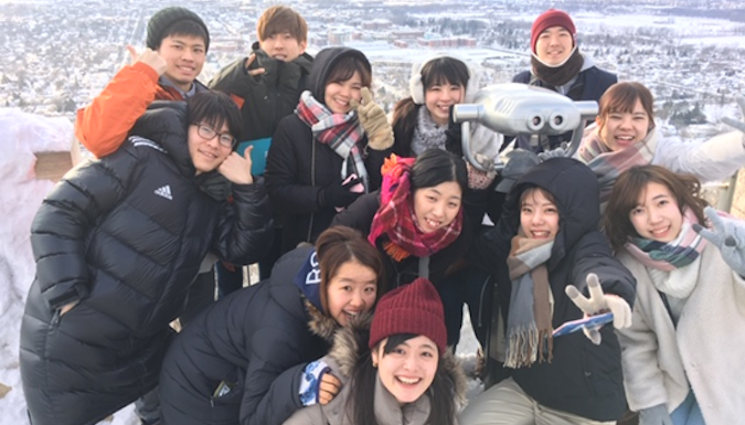 A group of education majors from the University of Teacher Education Fukuoka (UTEF) in Fukuoka, Japan stand in front of the University of Wisconsin-La Crosse sign.