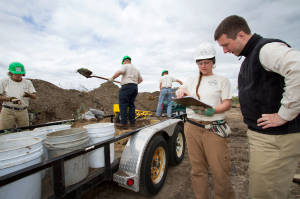 Image of Matthew Brantner discussing plans with Andrea Grant, in the background, other crew members are shoveling dirt.