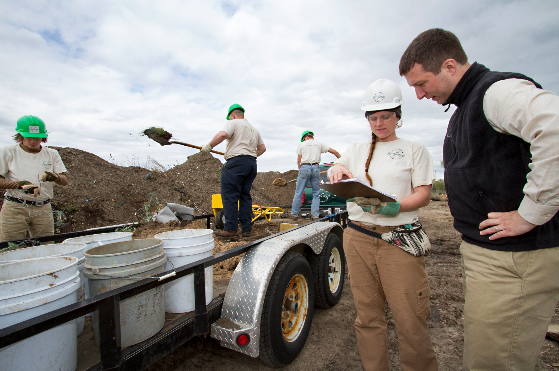 Image of Matthew Brantner discussing plans with Andrea Grant, in the background, other crew members are shoveling dirt. 