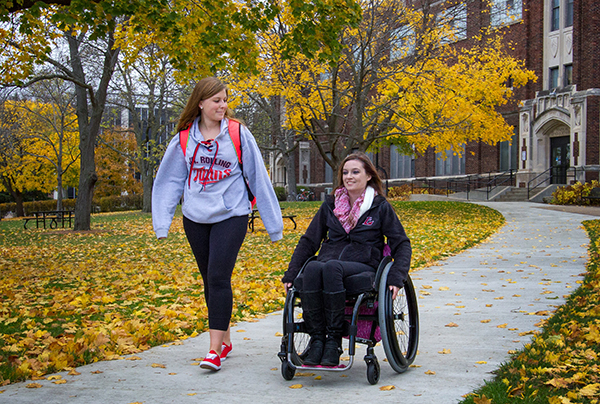 Image of Jordan Smith walking alongside Chantel Banks in her wheelchair on the UW-L campus. 