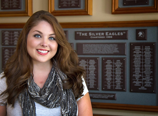 Image of Gina Schultz in front of a plaque that says Silver Eagles 