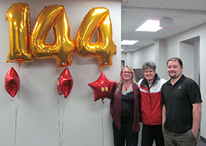 Photo of balloons with 144 and three people.