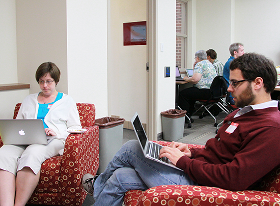 Image of David Mindel and Kate Russell sitting in chairs, typing on laptops. 