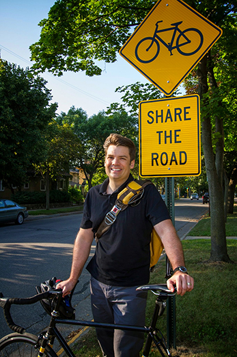 Image of James Longhurst standing with his bike near a "share the road" sign. 