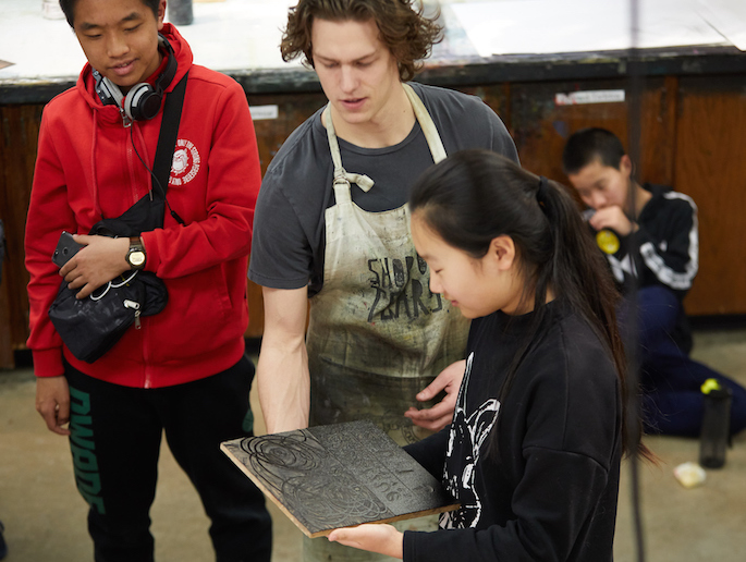 A UWL student holds a plate that is etched in front of a Chinese middle school student who is looking at the design.