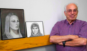 Retired physician Bill Kader standing next to two portraits he drew.