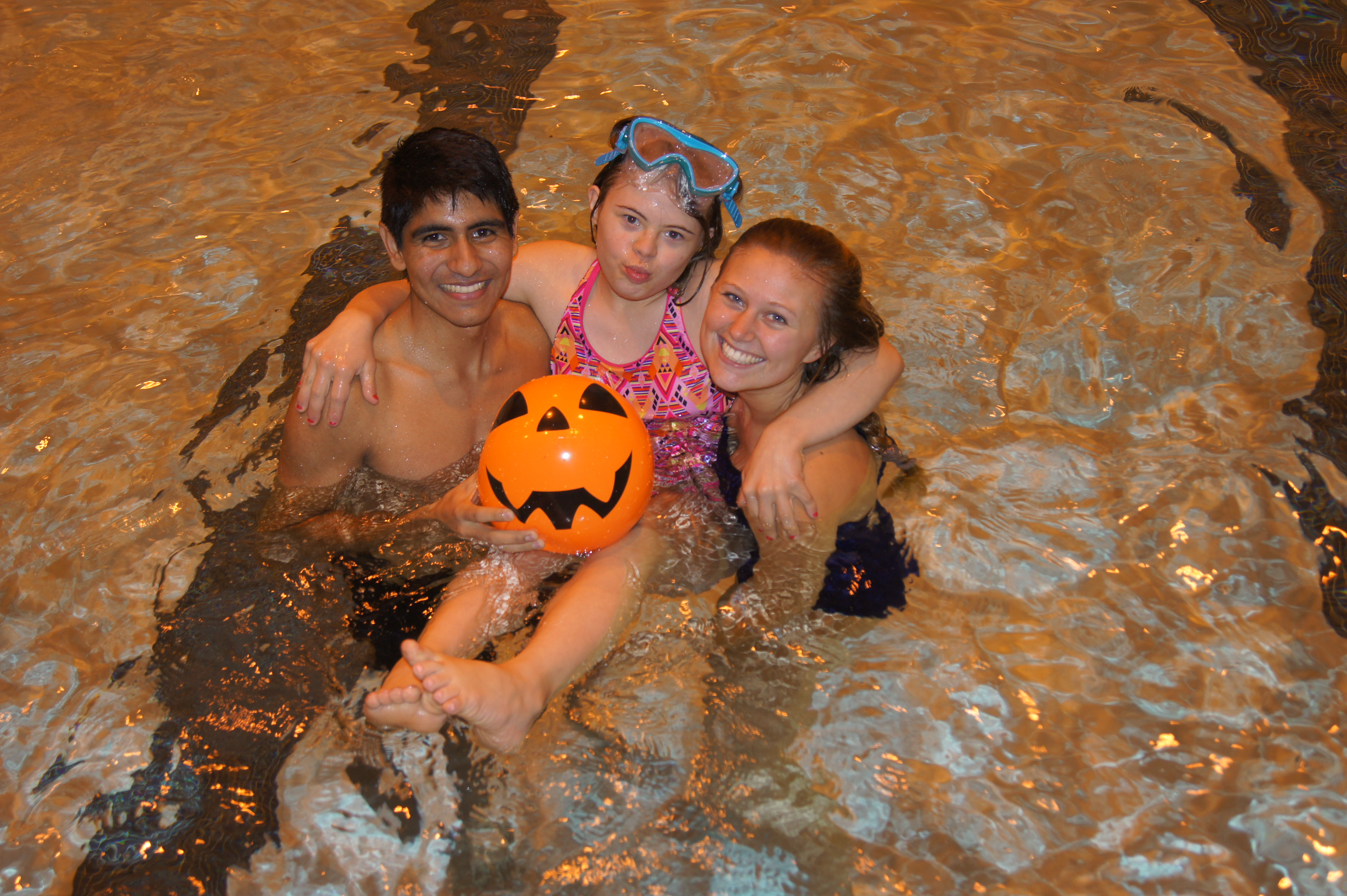 Two University Students play in the pool with a girl with a disability.