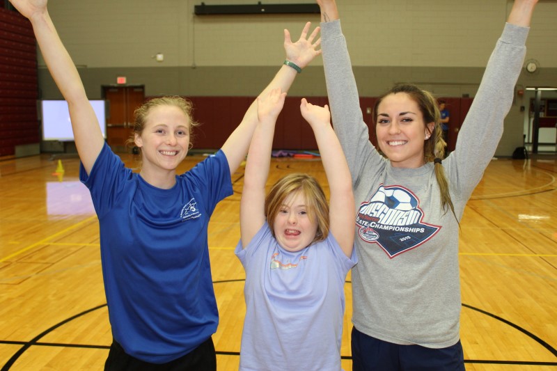 Two Physical Education Teaching Minors raise their hands to celebrate with a child with a disability.