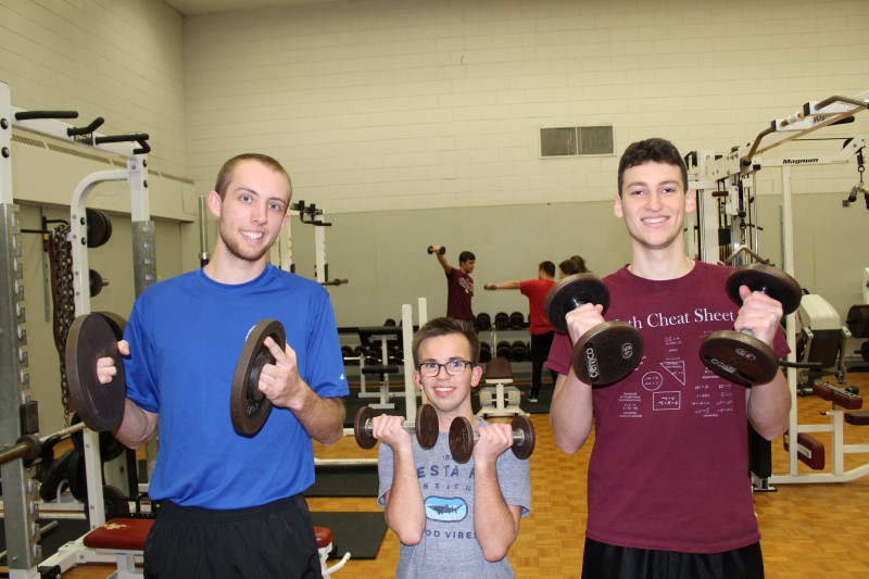 Two University Students lift weights with a boy with a disability.