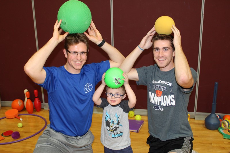 Two Adapted Physical Education Teaching Minors and a child with a disability hold their balls above their heads and smile.
